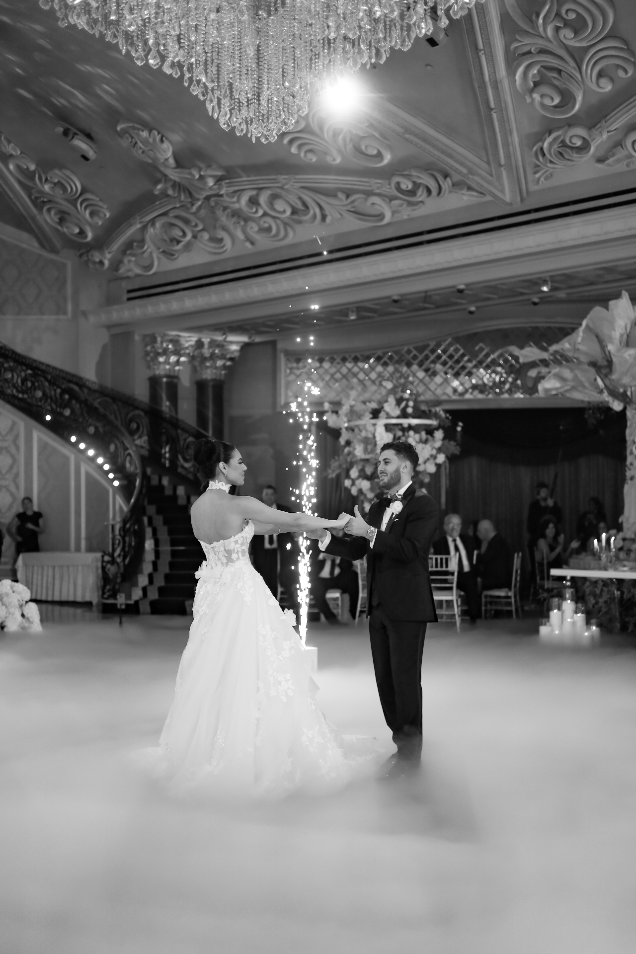Black and white photo of the bride and groom holding hands as fountain sparklers light up the dance floor