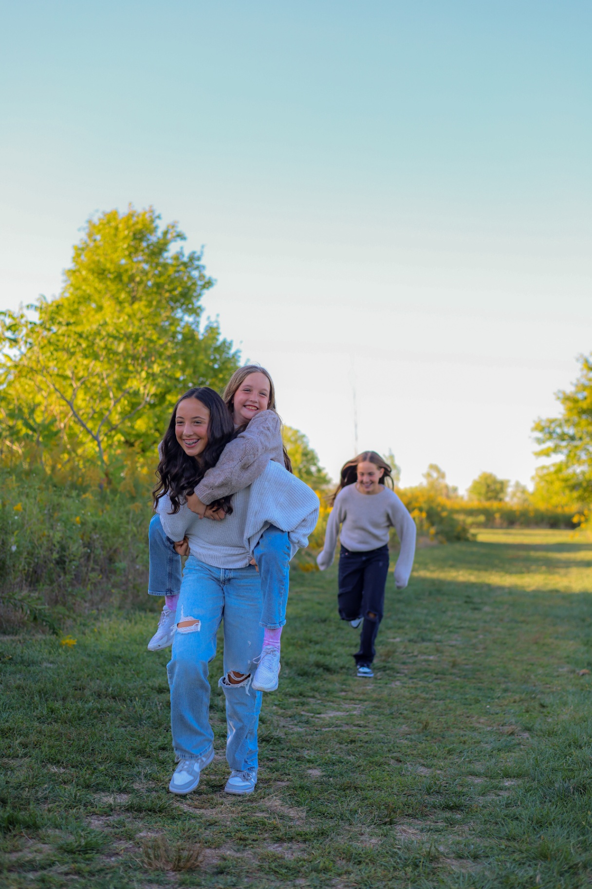 Sisters running through a grassy meadow giving piggyback rides at sunset