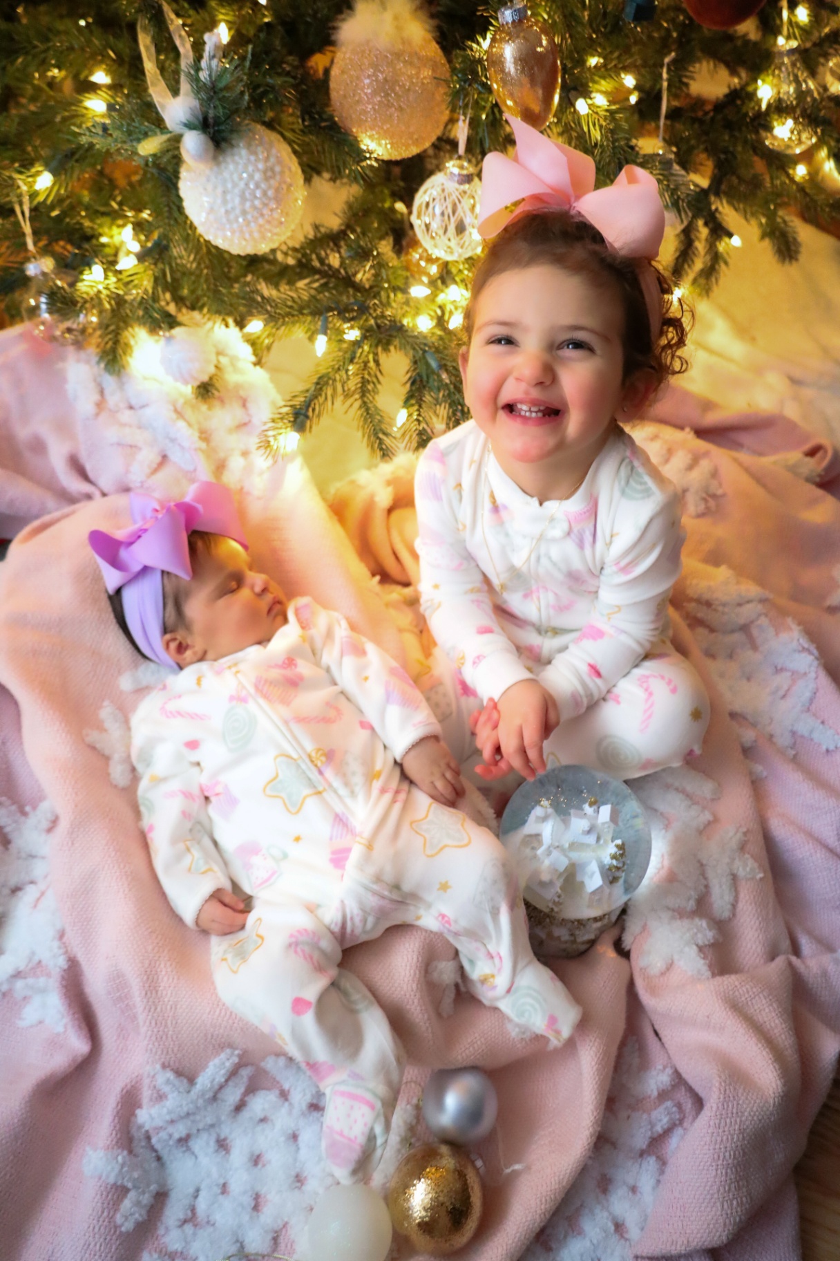 Big sister beaming next to her sleeping newborn sister at Christmas