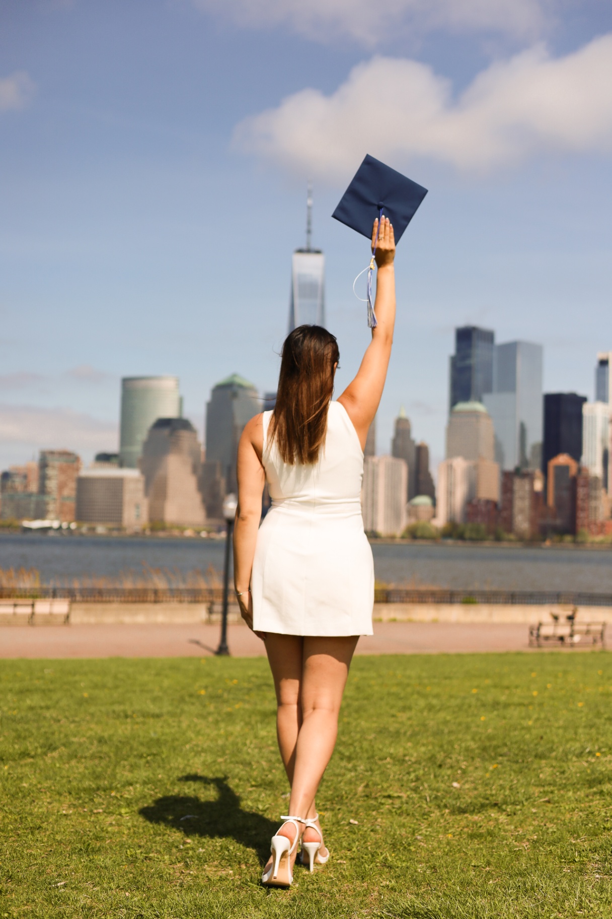 Graduate walking toward NYC skyline with cap raised