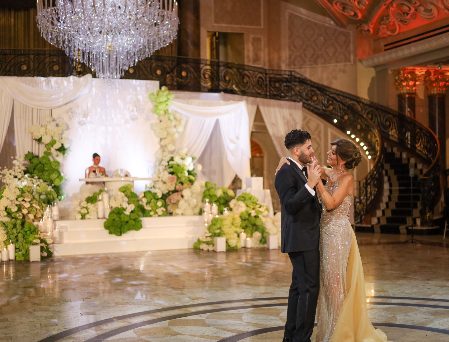 Mother and son sharing a dance in a grand ballroom with a sweeping staircase and hydrangeas