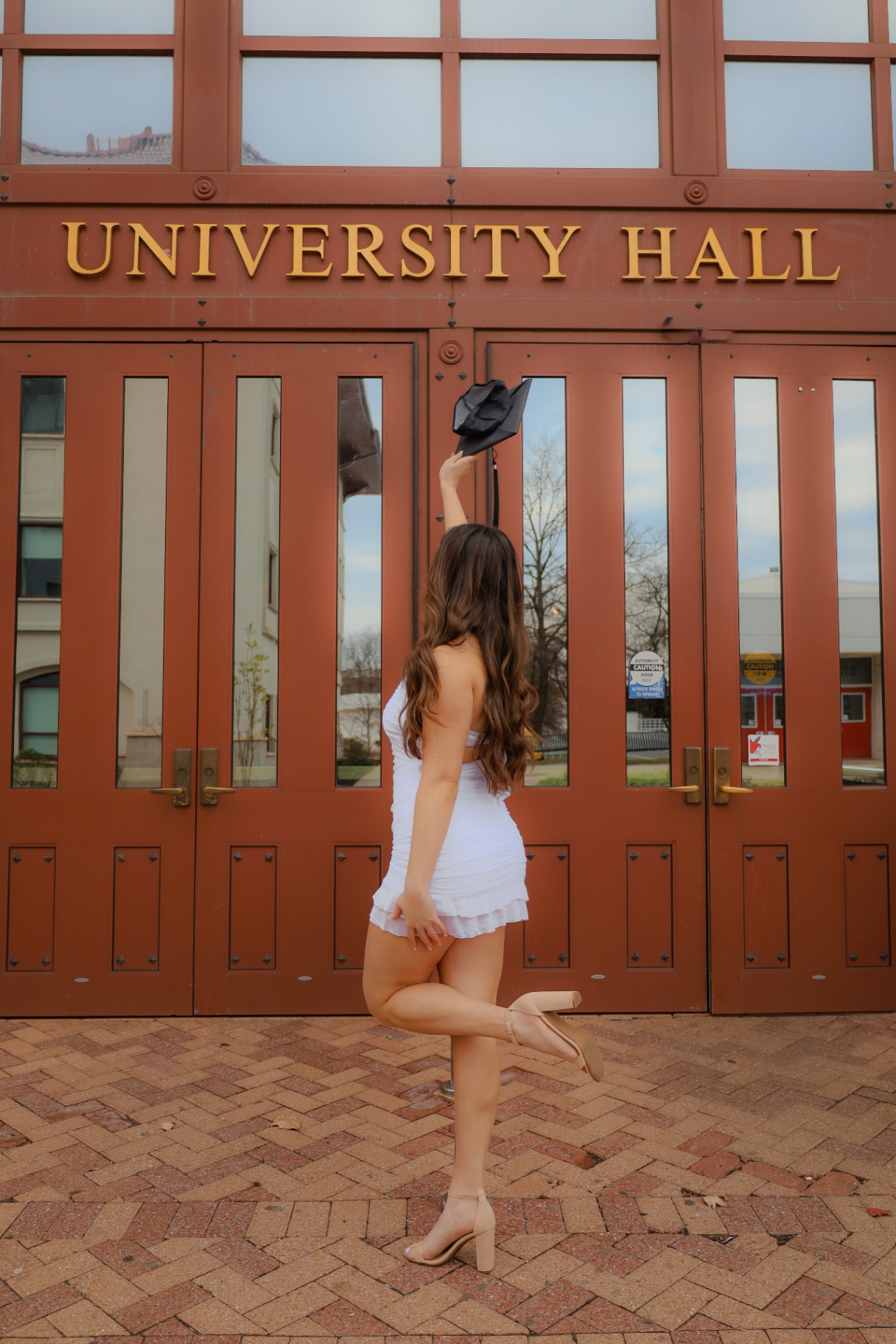 Graduate posing in front of University Hall doors with cap raised