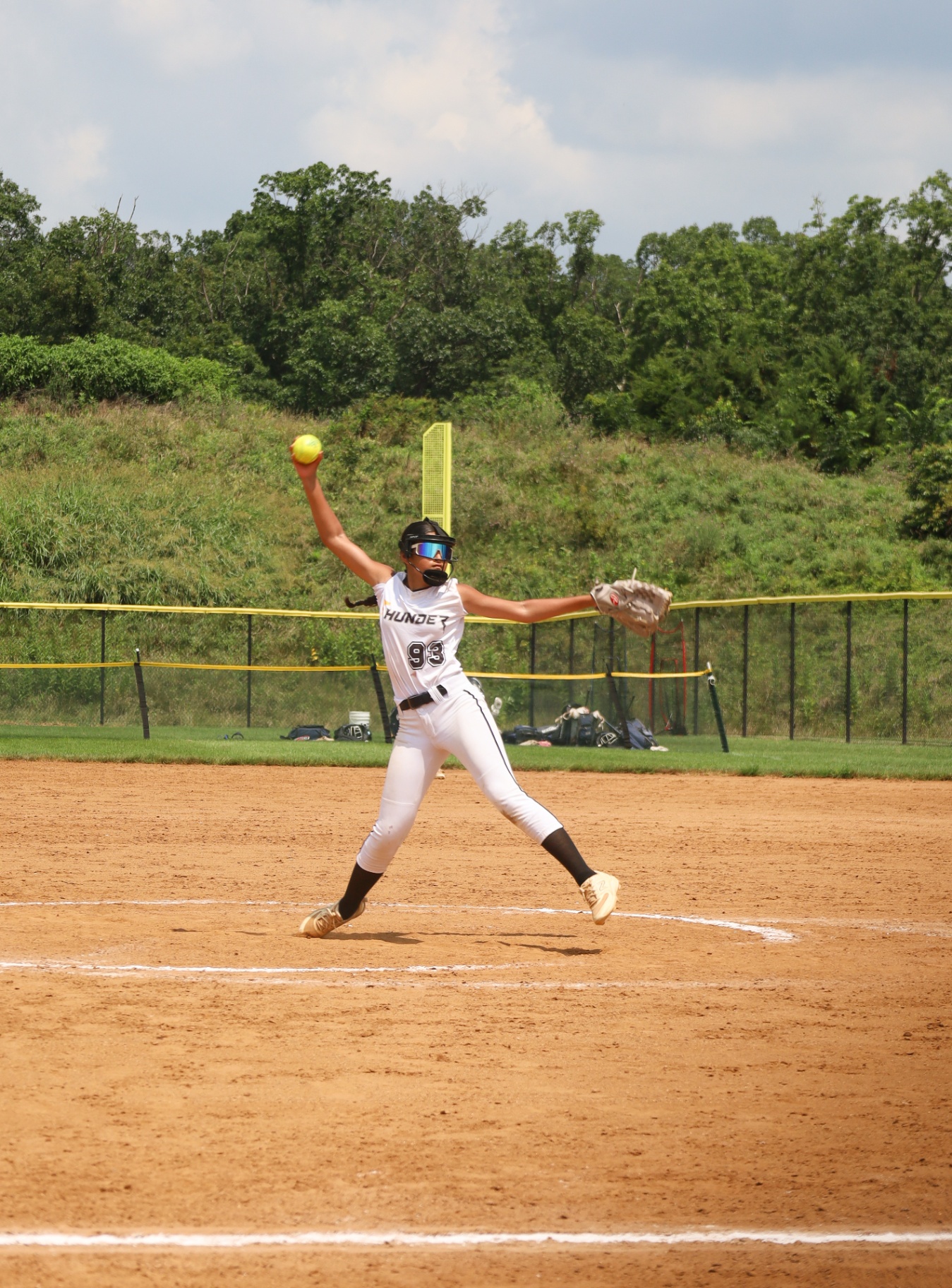 Softball pitcher in white Thunder jersey mid wind-up on the mound