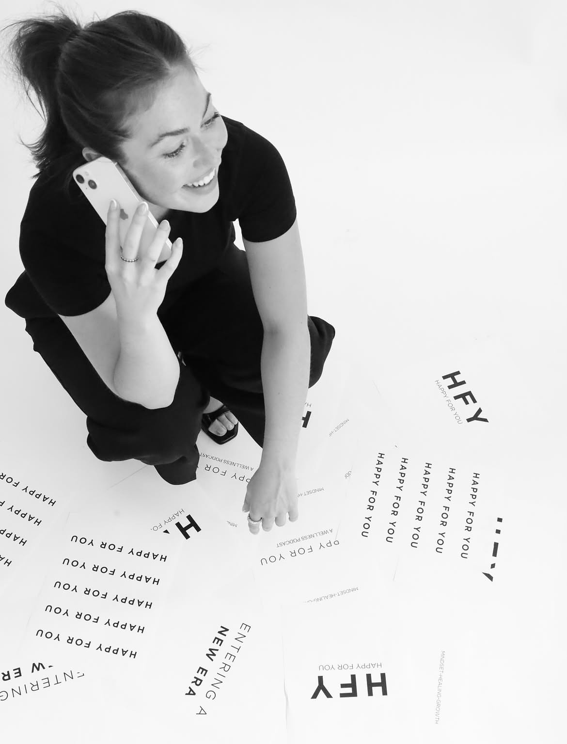 Black and white lifestyle branding portrait with Happy For You print pieces on the floor