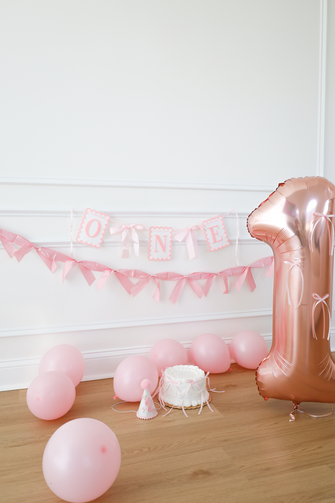 Pink first birthday setup with one banner, cake, party hat, and rose gold number one balloon