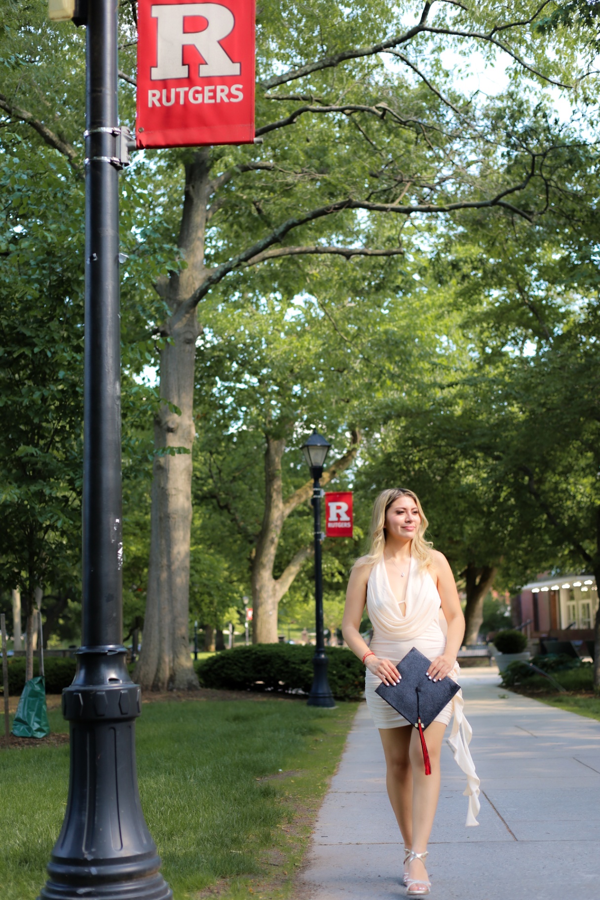Graduate walking down a tree-lined sidewalk beneath Rutgers banners