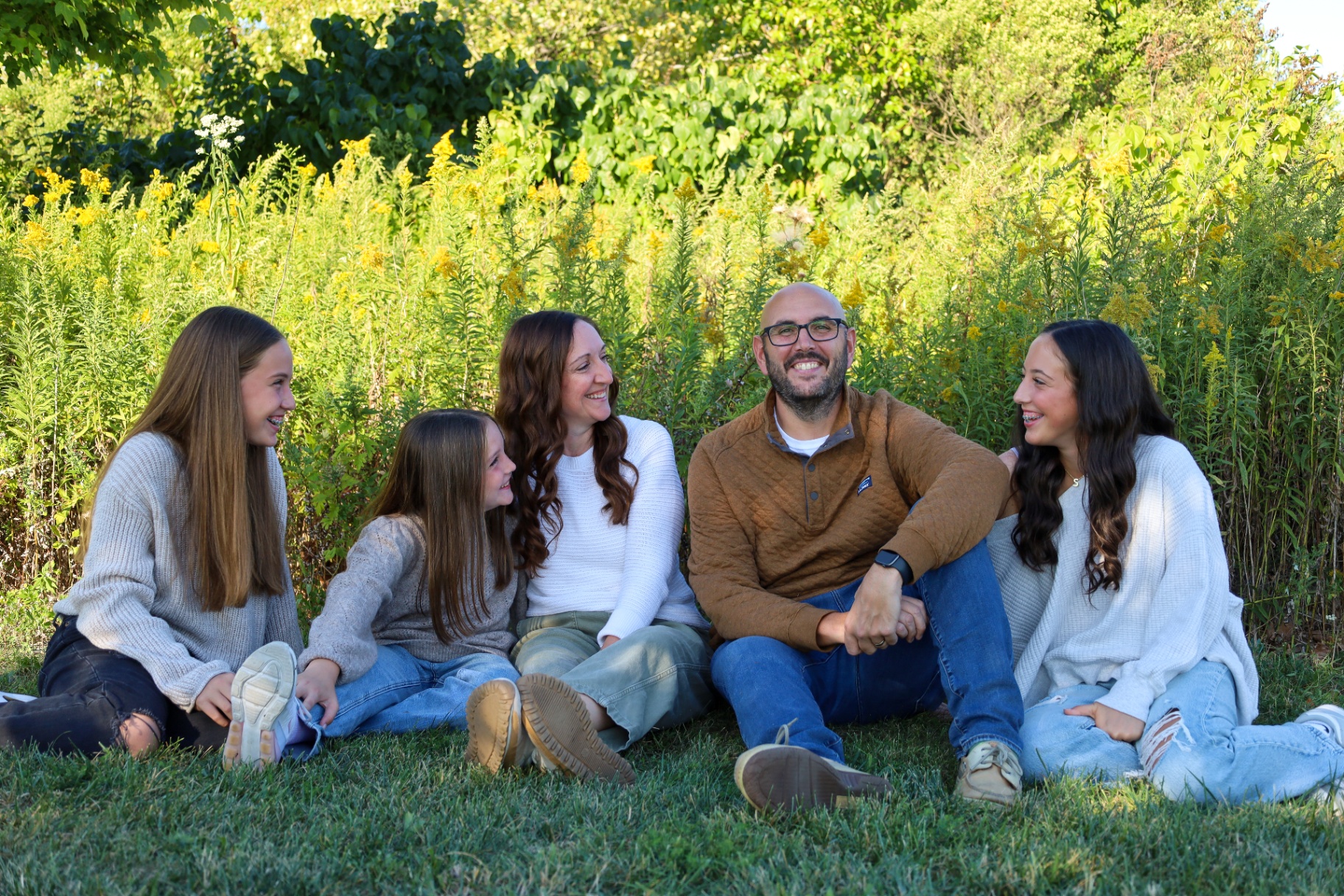 Family of five laughing together in a sunlit goldenrod field