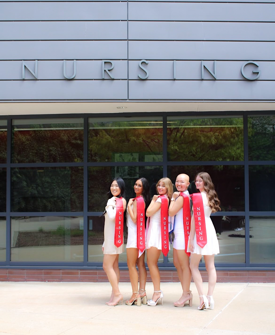 Group of nursing graduates lined up beneath the Nursing building sign