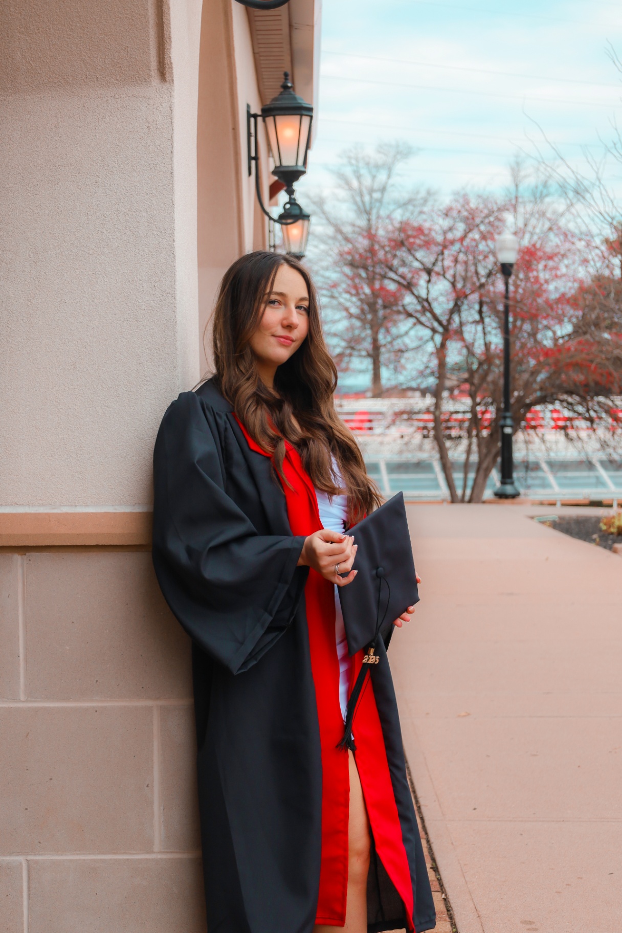 Nursing graduate leaning against a campus wall holding her cap