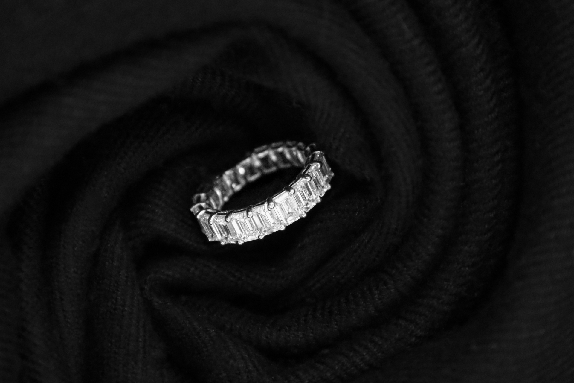 Emerald-cut diamond eternity band nestled in swirled black cashmere fabric