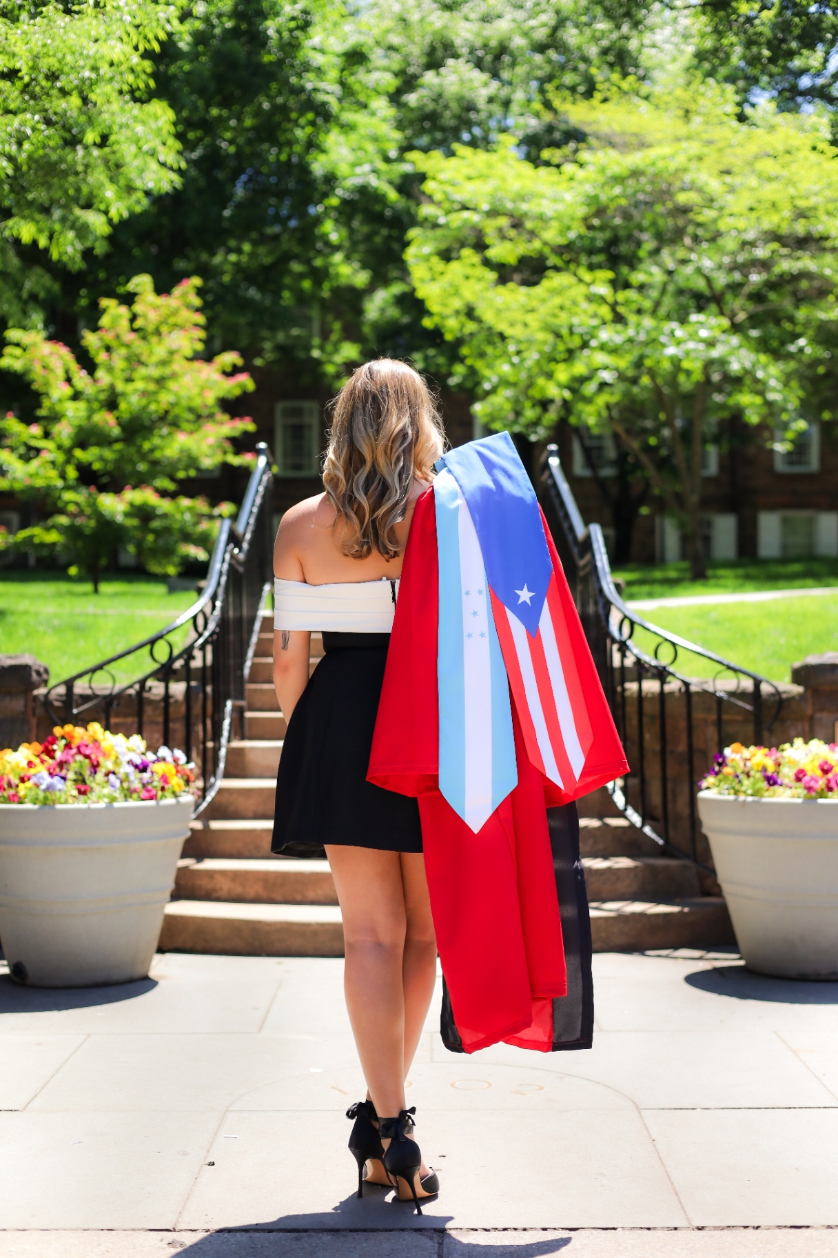 Graduate on campus steps draped in Puerto Rico and Honduras flags