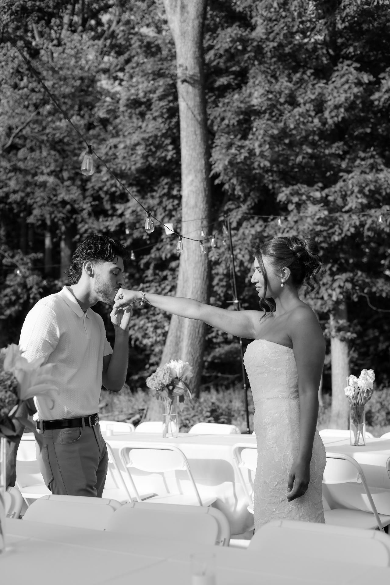 Black and white photo of the groom kissing the bride's hand at their outdoor wedding reception
