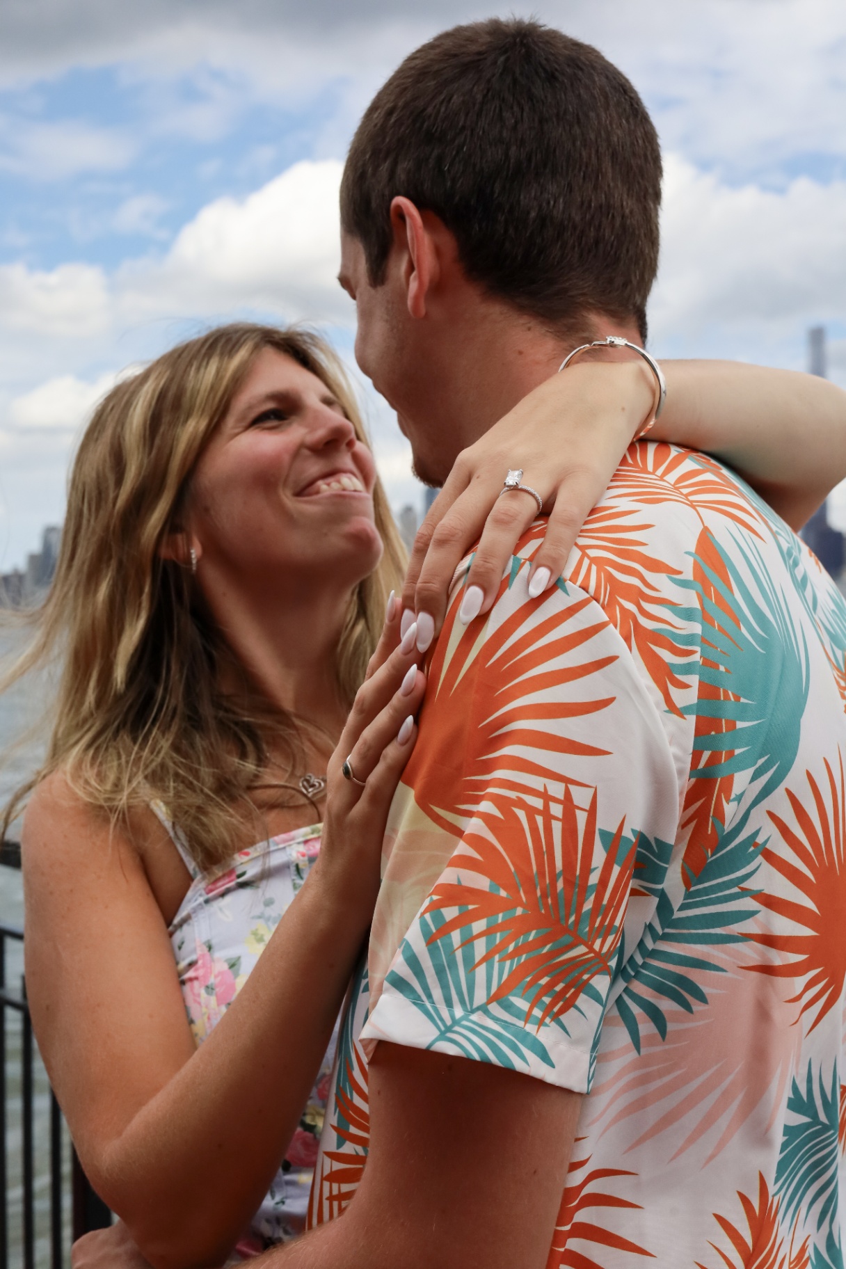Newly engaged couple embracing on a pier with the city skyline behind them