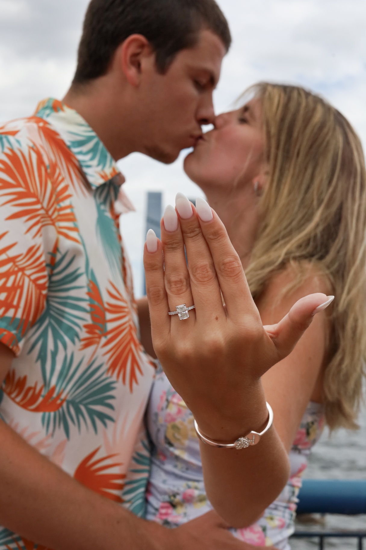 Engagement ring close-up as the couple shares a kiss by the water