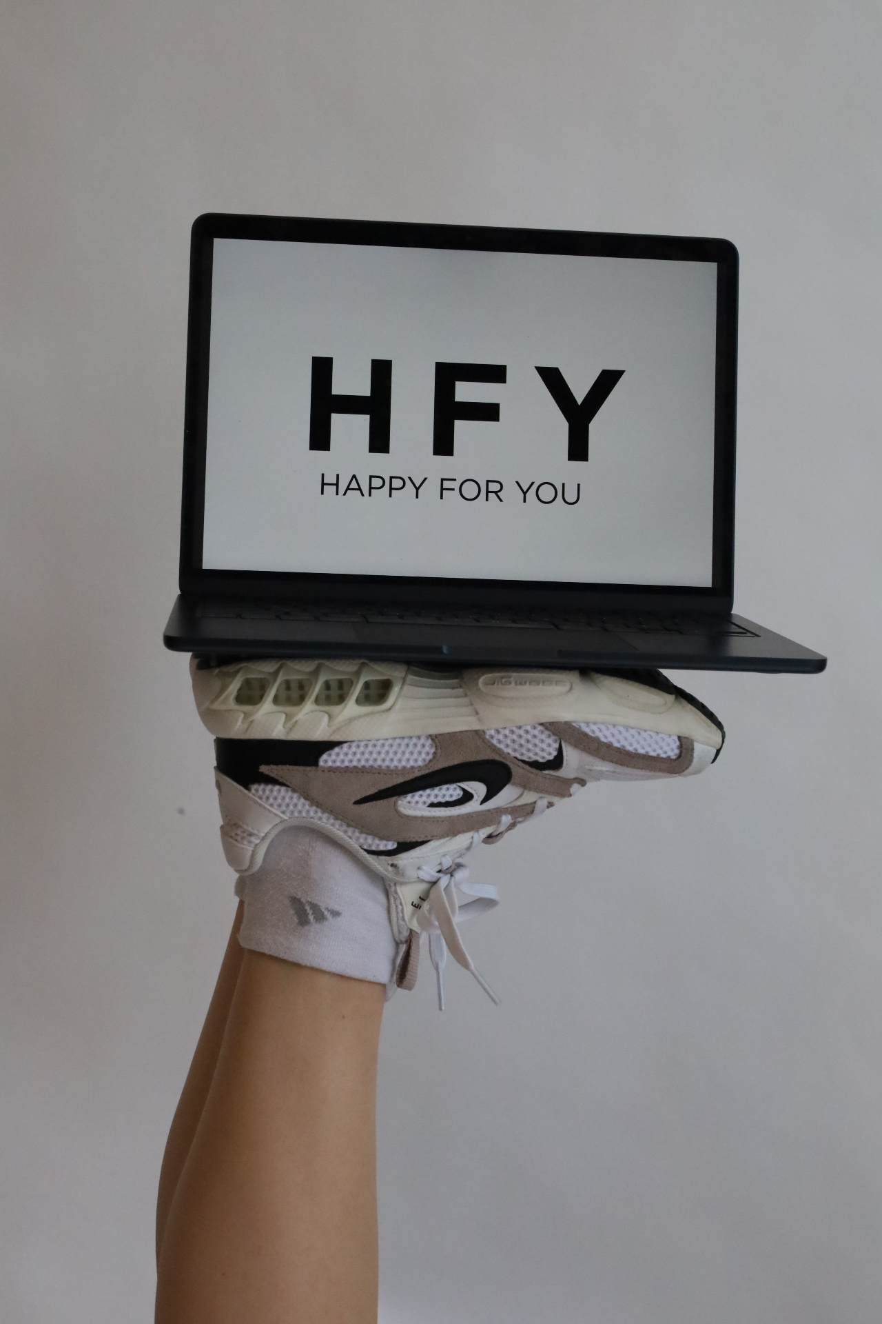Laptop showing HFY Happy For You logo balanced atop a Nike sneaker