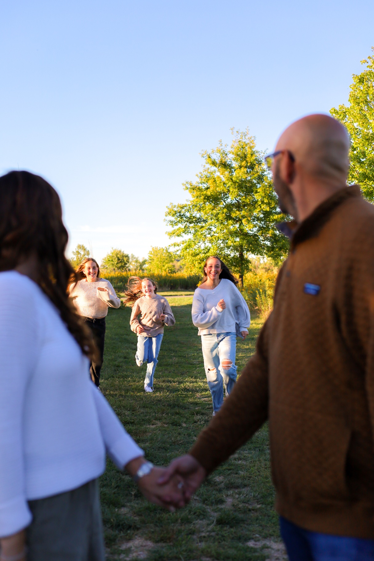 Daughters running toward mom and dad who are holding hands in a field
