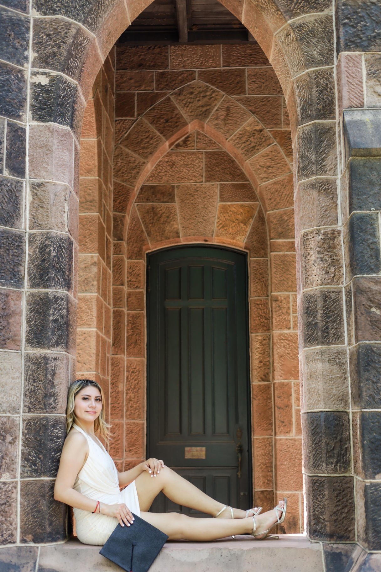 Graduate seated inside a Gothic stone archway on campus