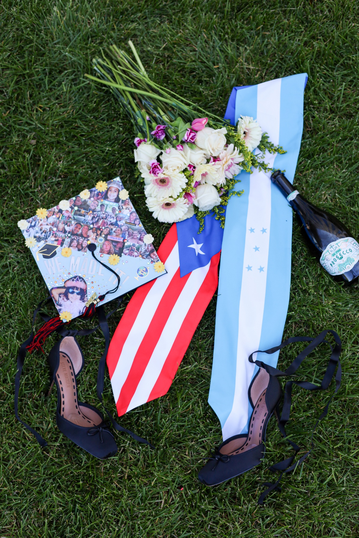 Flat lay of cap, flowers, flags, heels and prosecco on grass