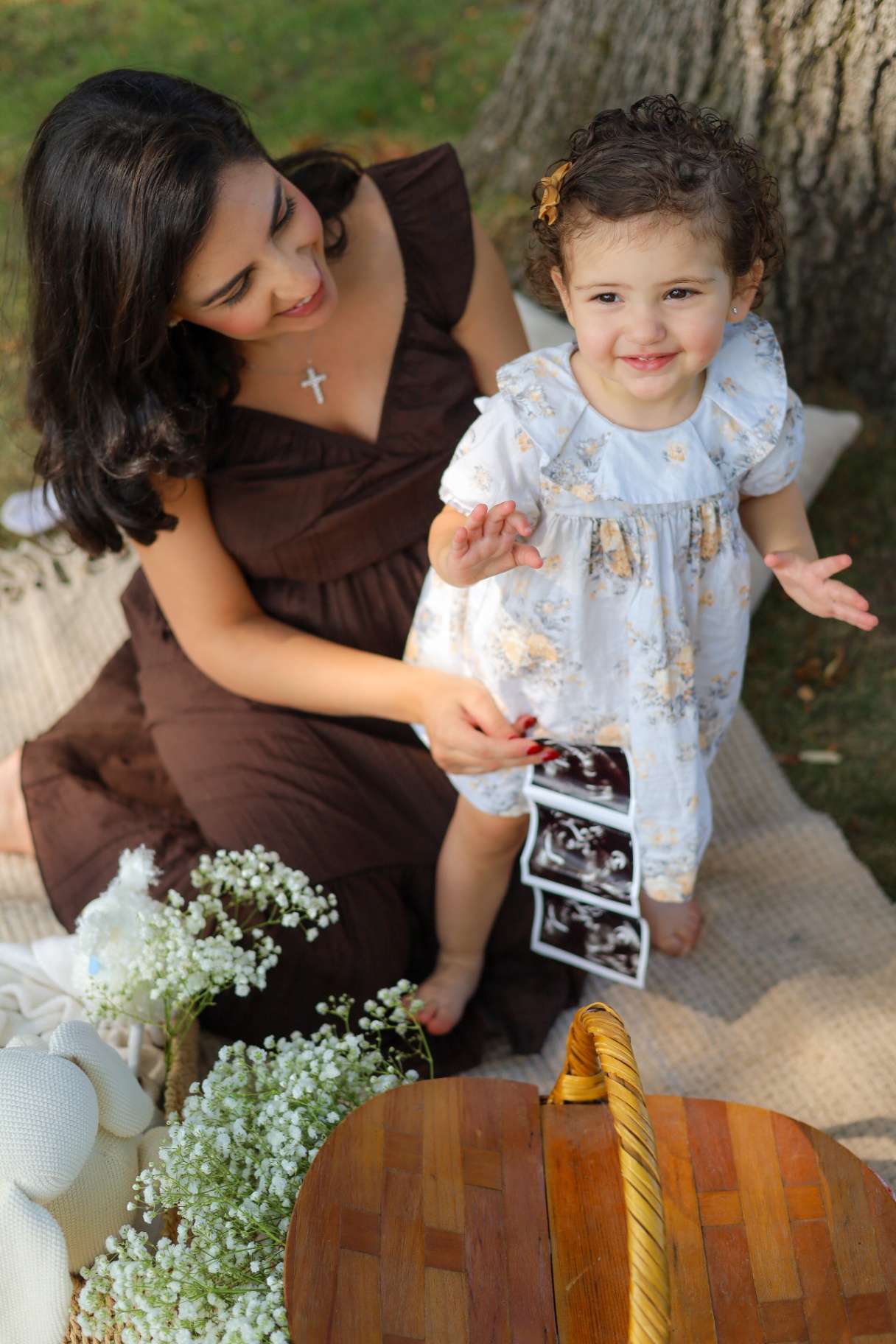 Mother smiling at her toddler daughter who is holding ultrasound photos in the grass