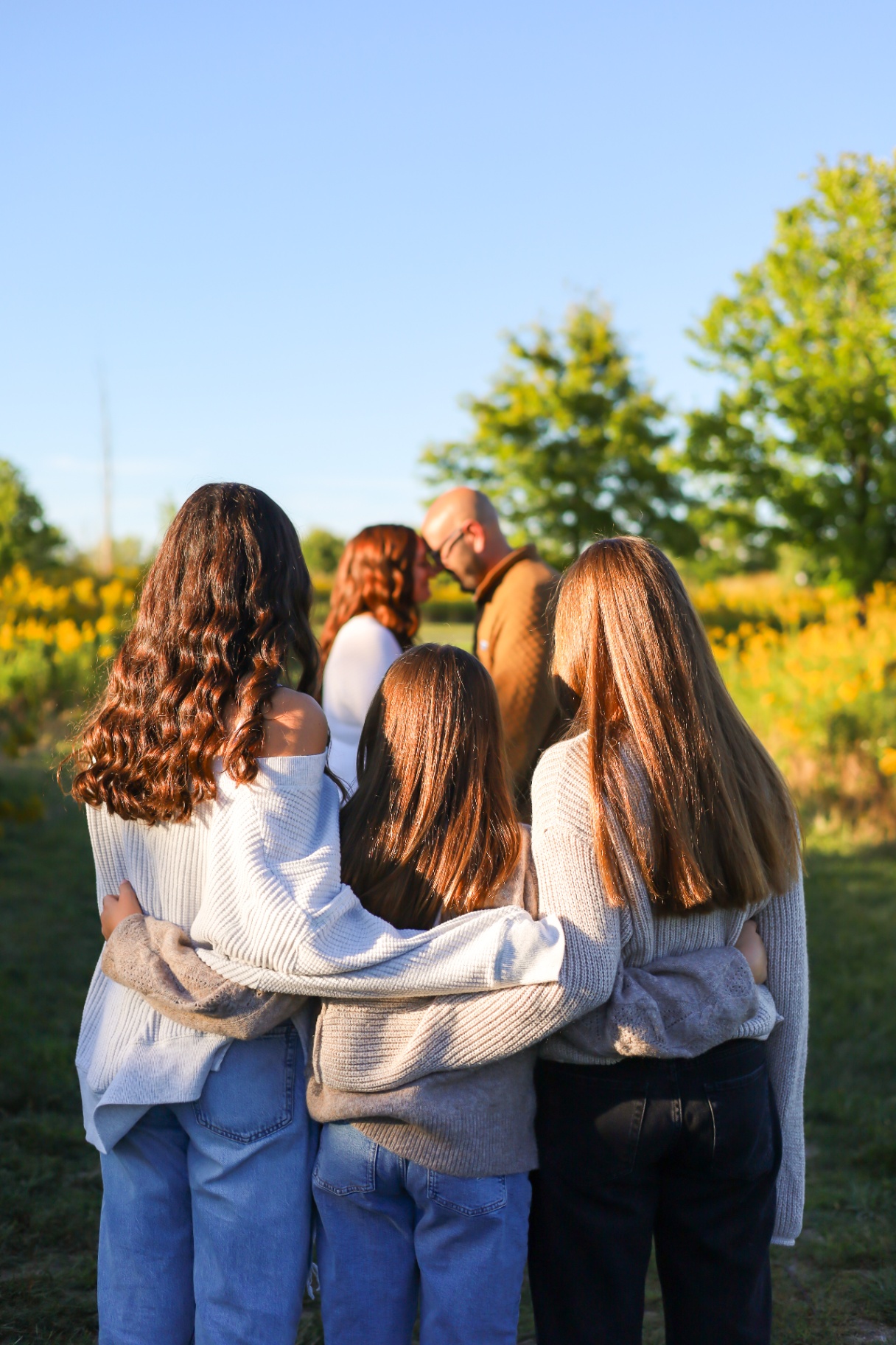 Daughters embracing while parents share a moment in a sunflower field
