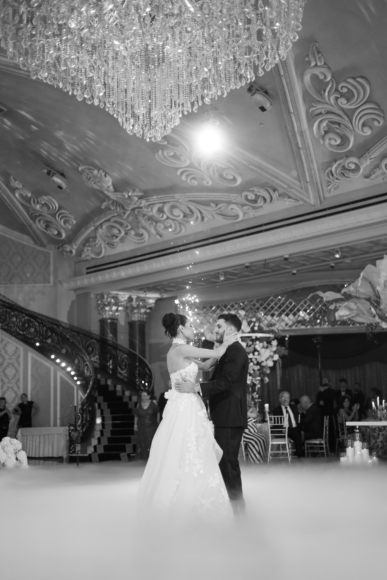 Black and white portrait of the bride and groom embracing during their first dance with sparklers behind them