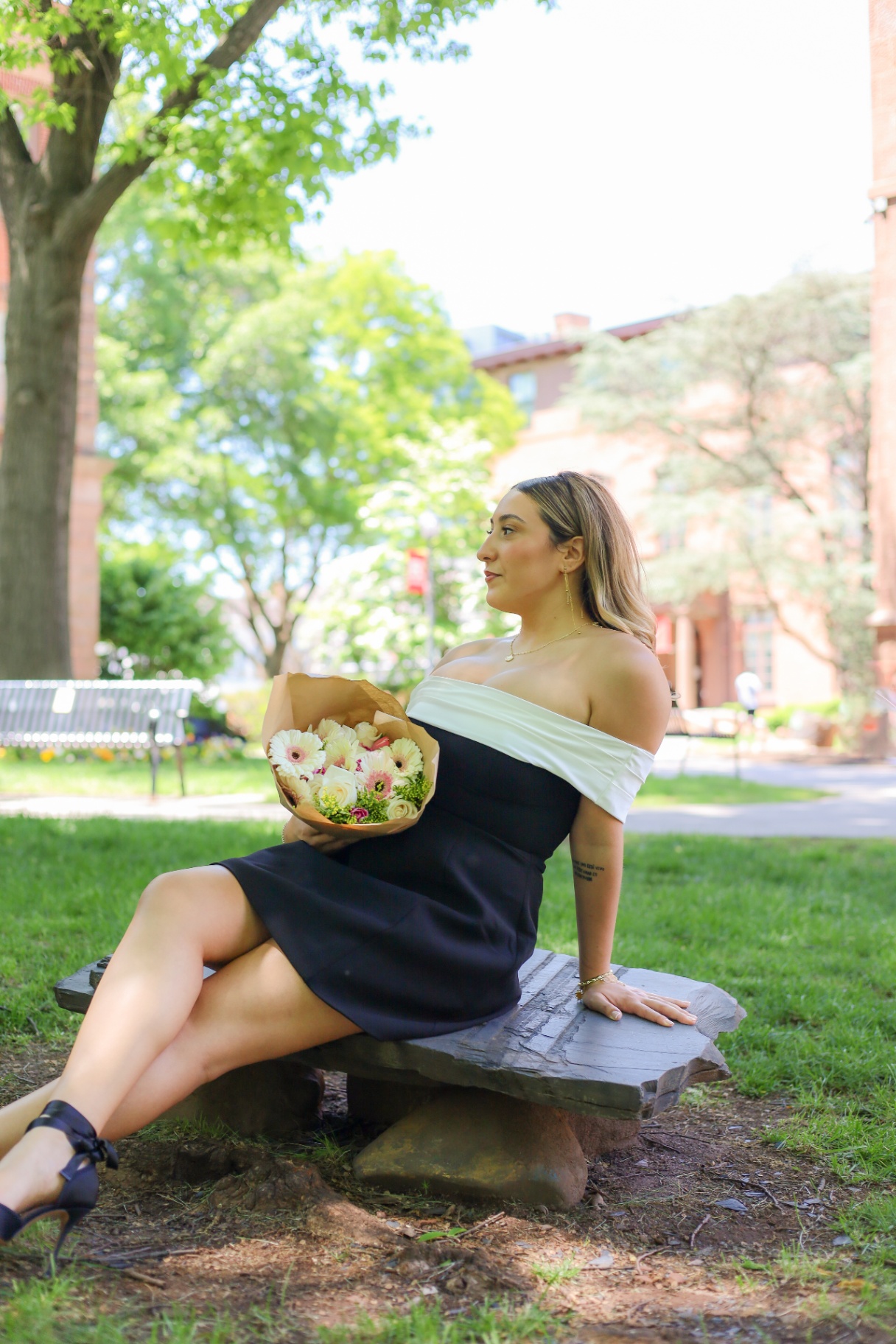 Graduate seated on stone bench holding a bouquet