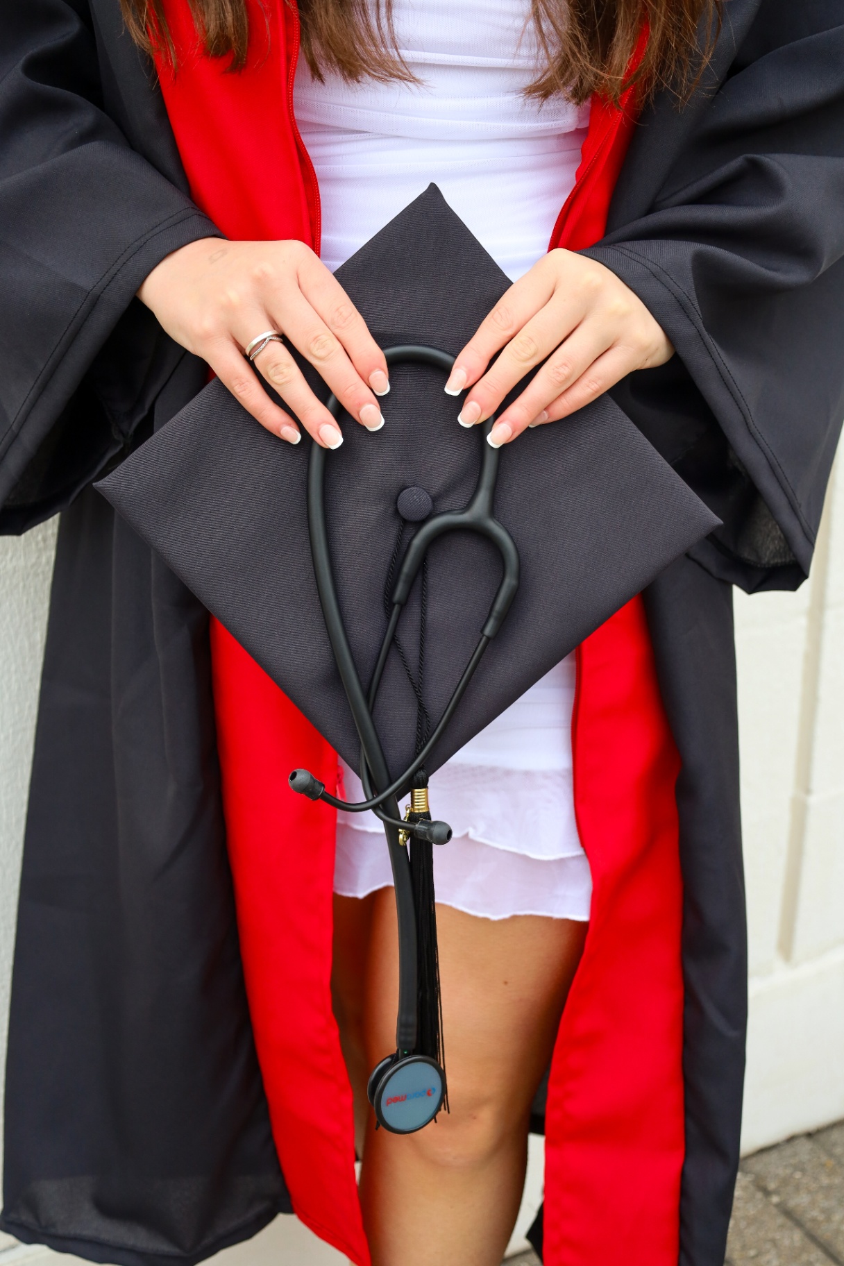 Close-up of graduation cap with stethoscope and manicured hands