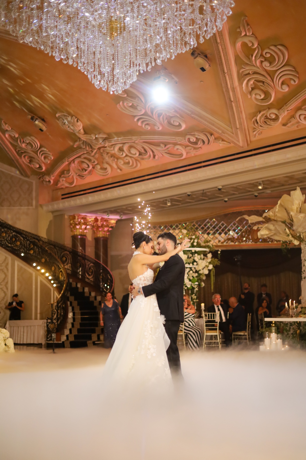 Bride and groom's first dance under a crystal chandelier with sparklers and dancing on the clouds