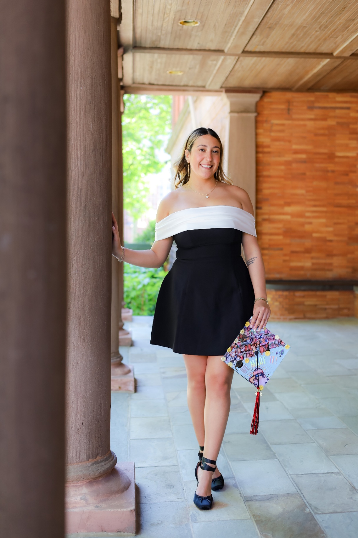 Graduate in black and white dress beside sandstone column