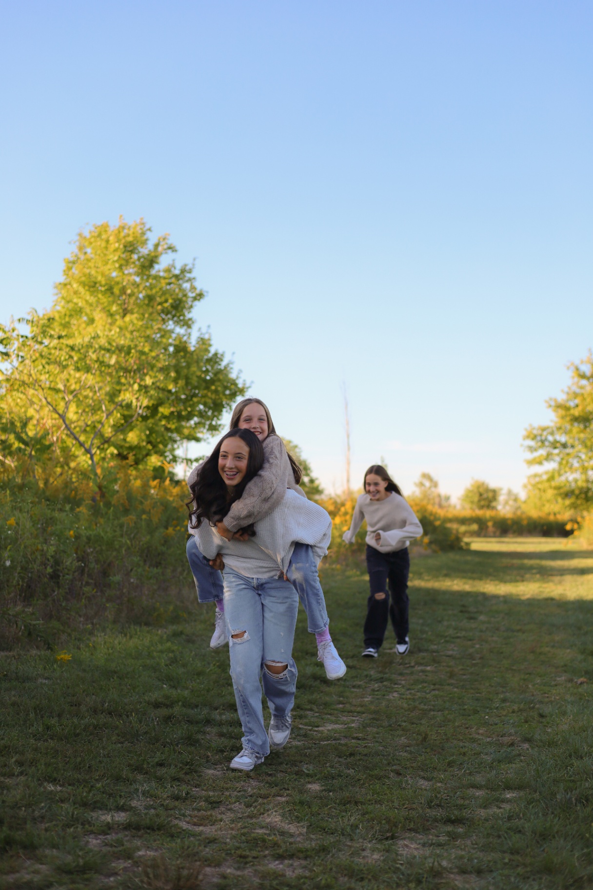 Three sisters playing and piggybacking down a sunlit field path