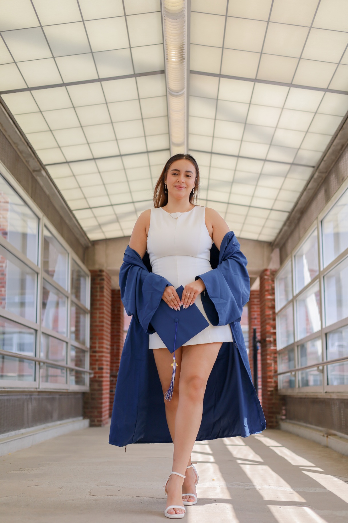 Graduate holding cap inside a bright glass walkway