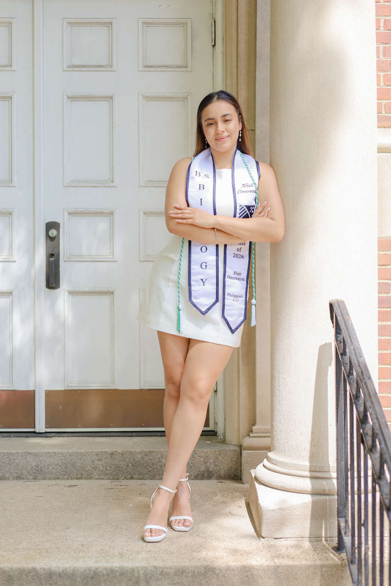 Biology graduate Class of 2026 in white dress with stole leaning against a column