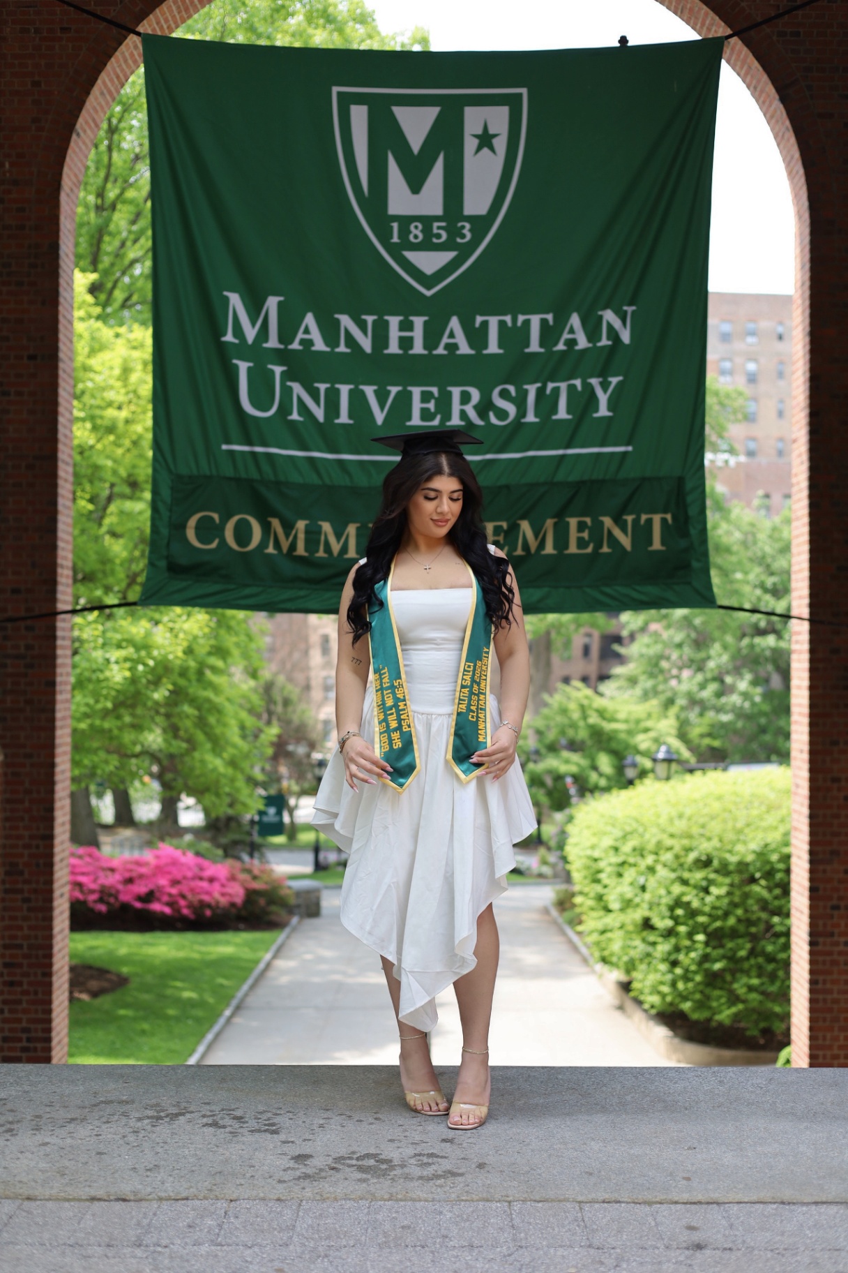Manhattan University graduate posing beneath the commencement banner