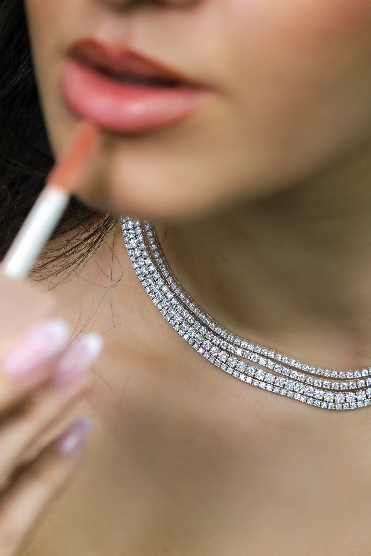 Beauty close-up with glossy lips and a layered crystal necklace during makeup application