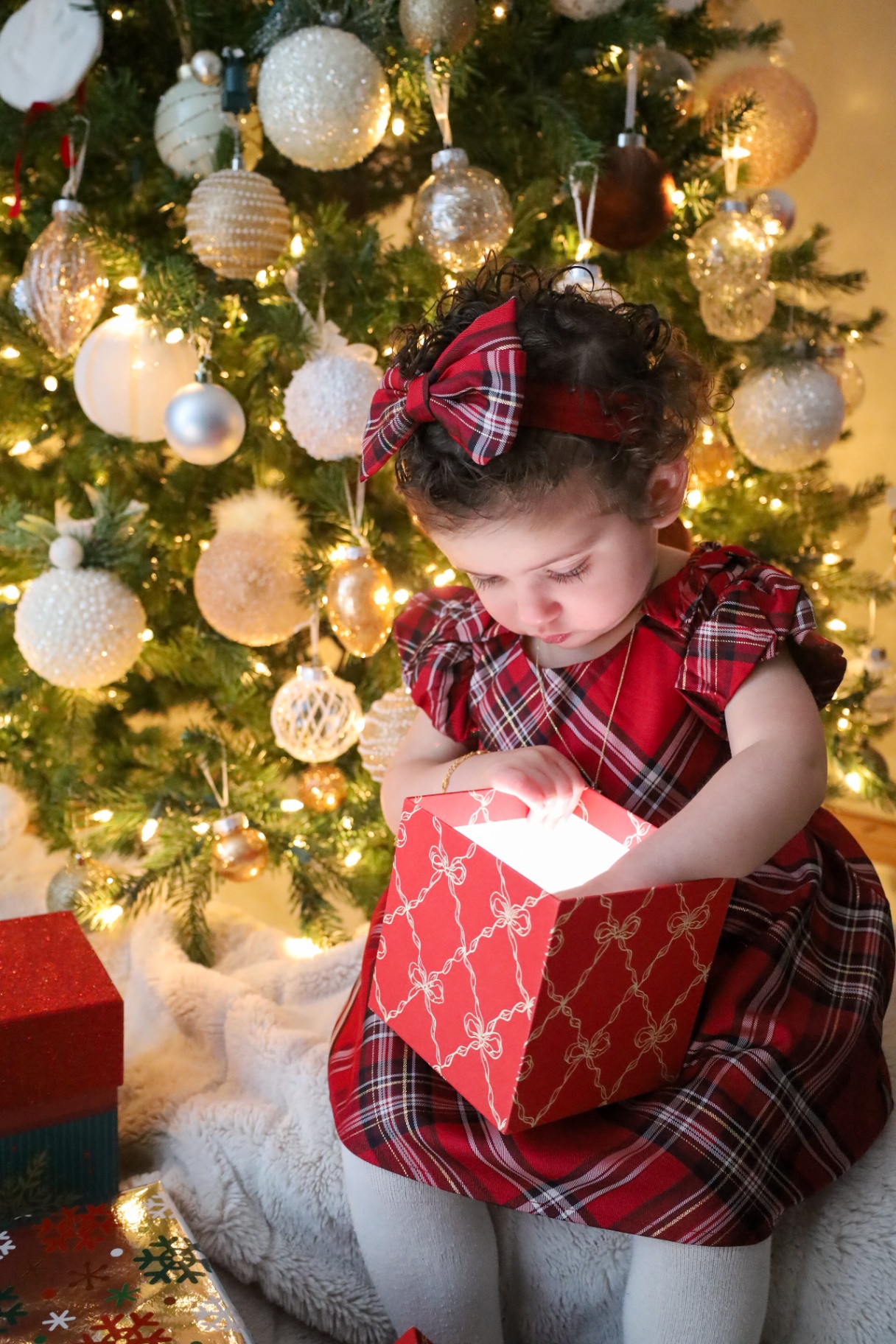 Little girl in plaid opening a softly glowing gift box under the tree
