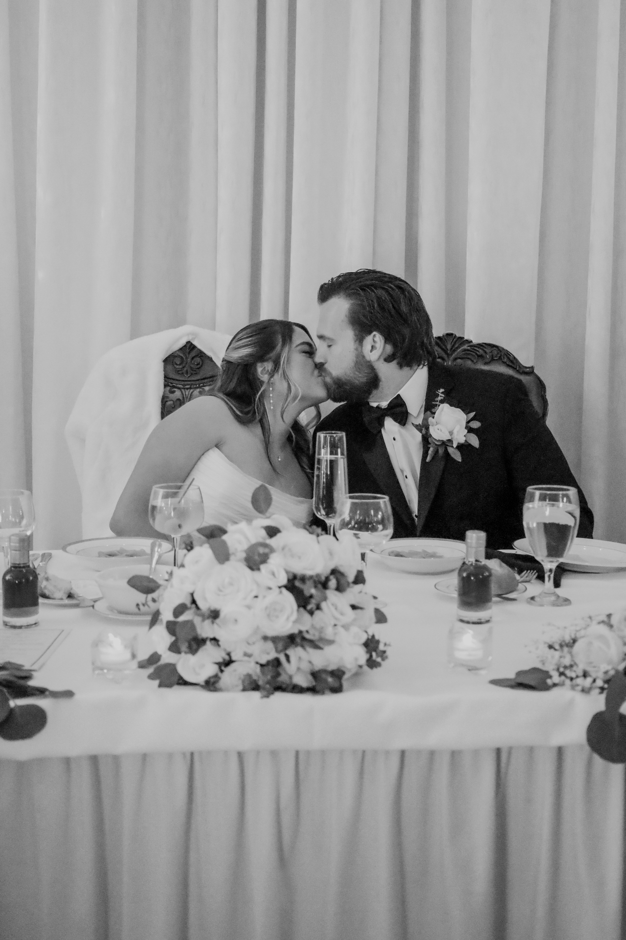 Black and white portrait of the bride and groom sharing a kiss at the sweetheart table