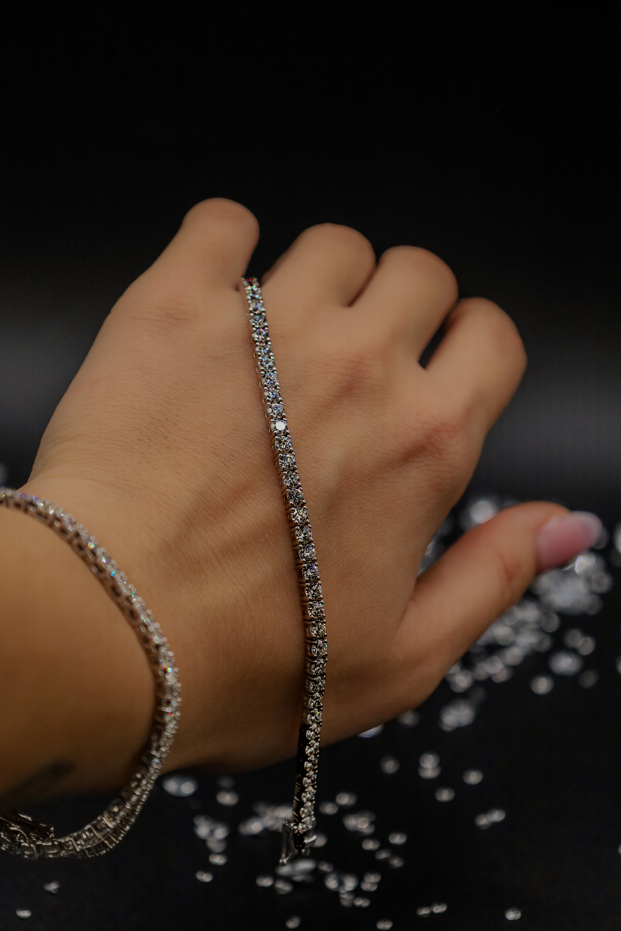 Close-up of a hand displaying a sparkling bracelet over a dark reflective background