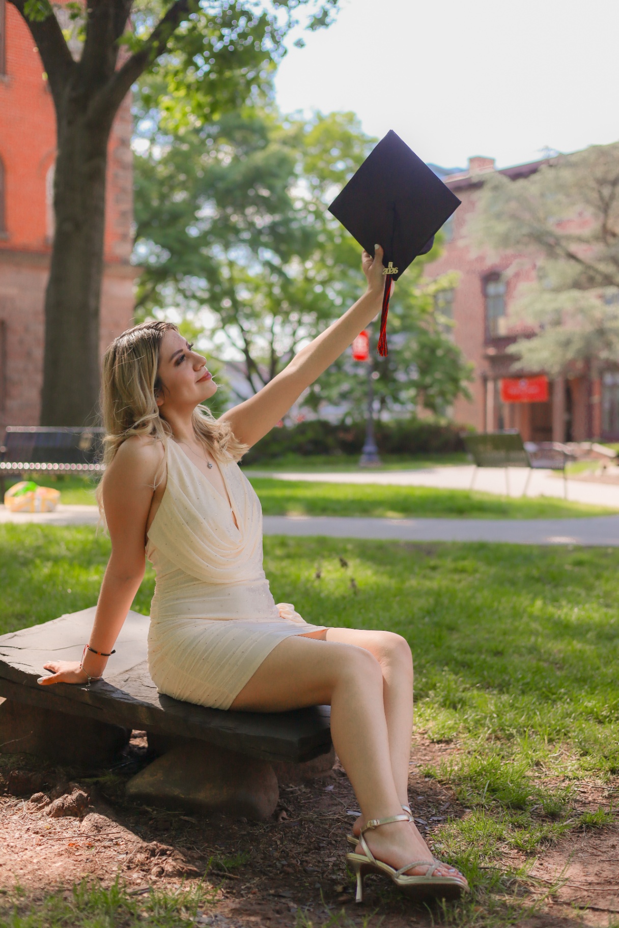Graduate seated on a bench lifting her cap on Rutgers campus