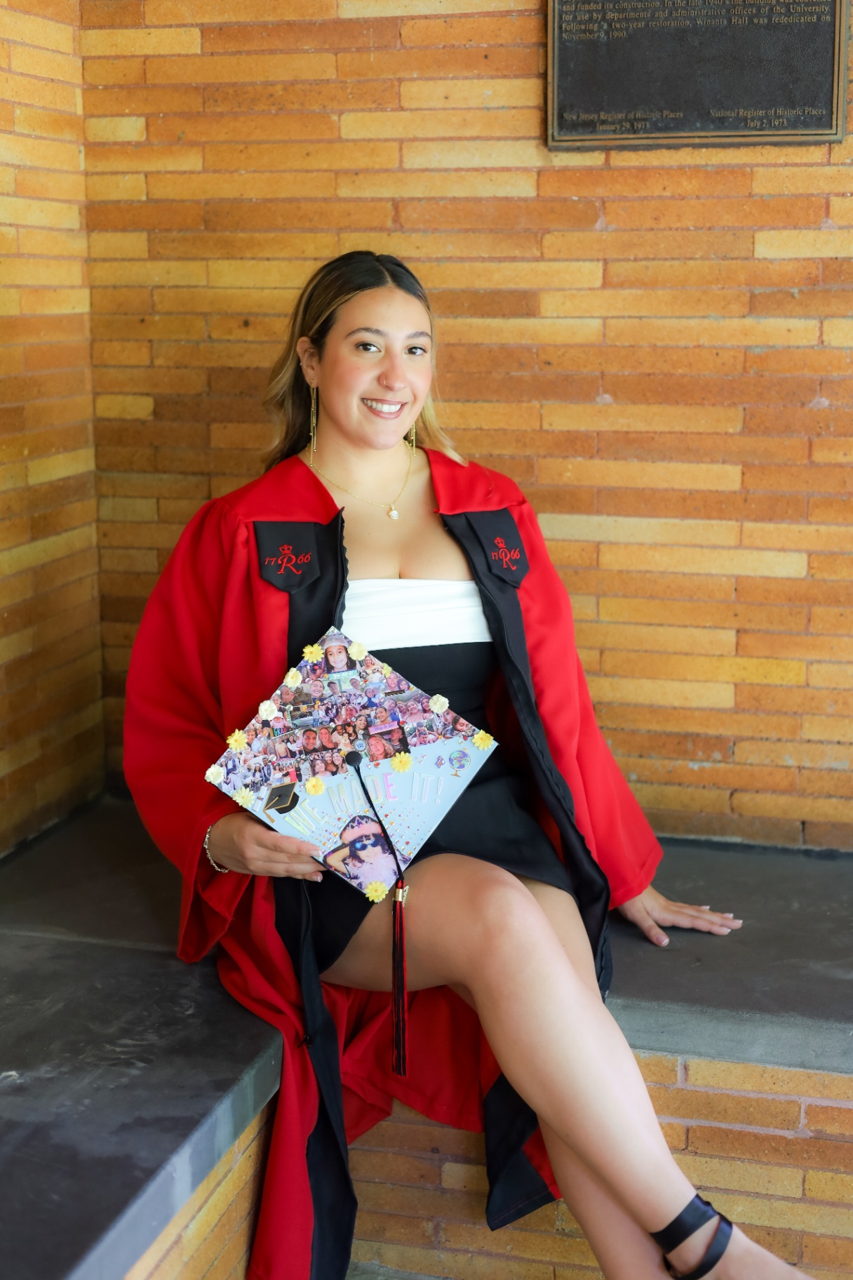 Graduate in red Rutgers gown holding decorated cap on brick steps