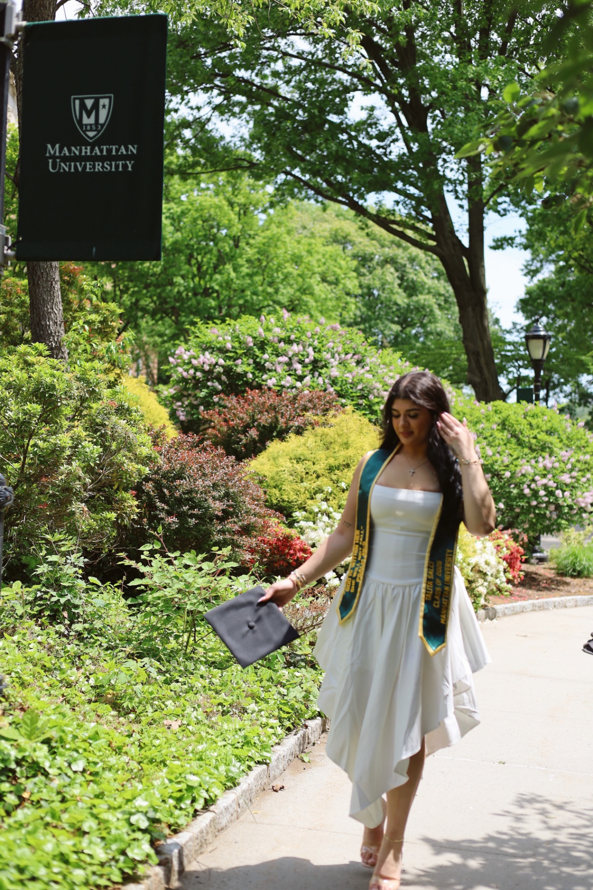 Manhattan University graduate walking along a garden path with cap in hand