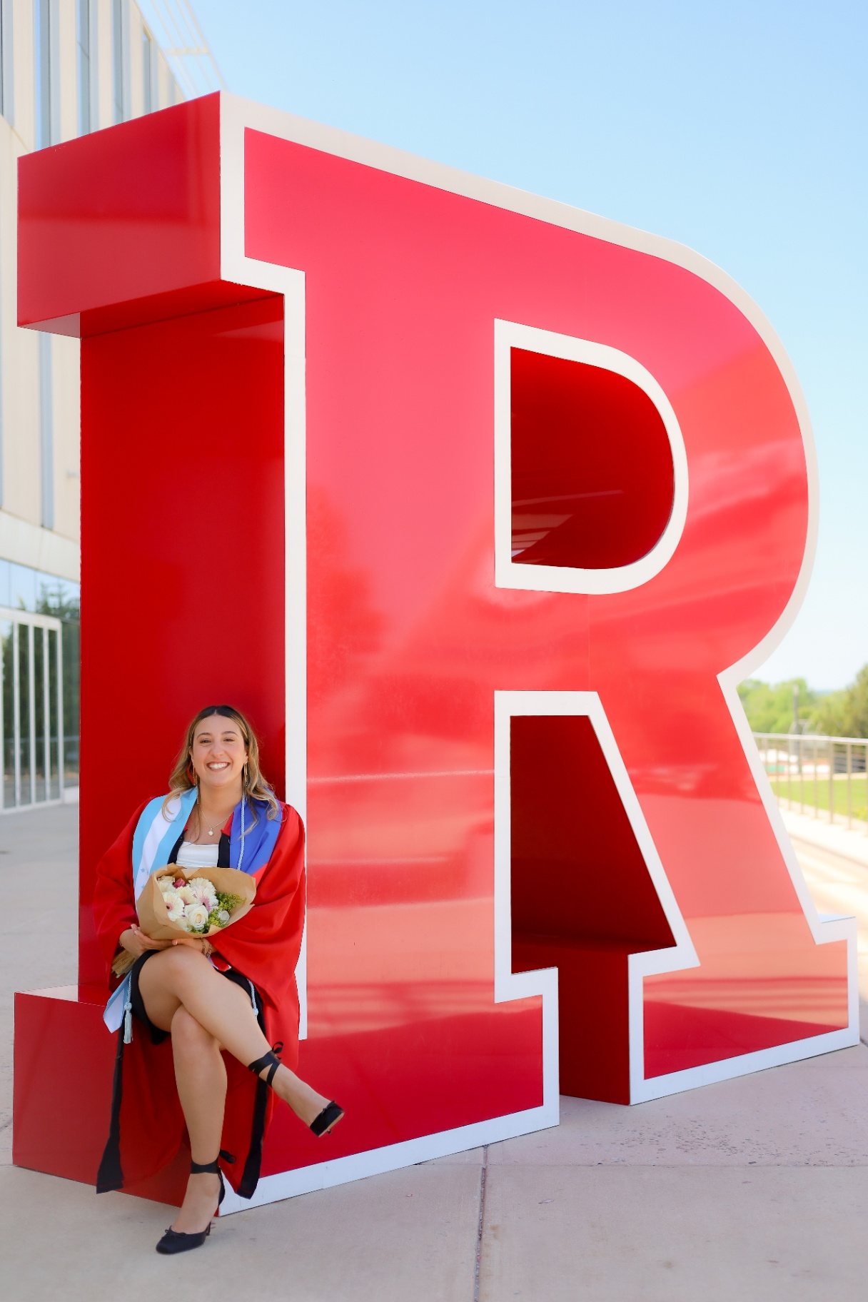Rutgers graduate seated inside the giant red R sculpture