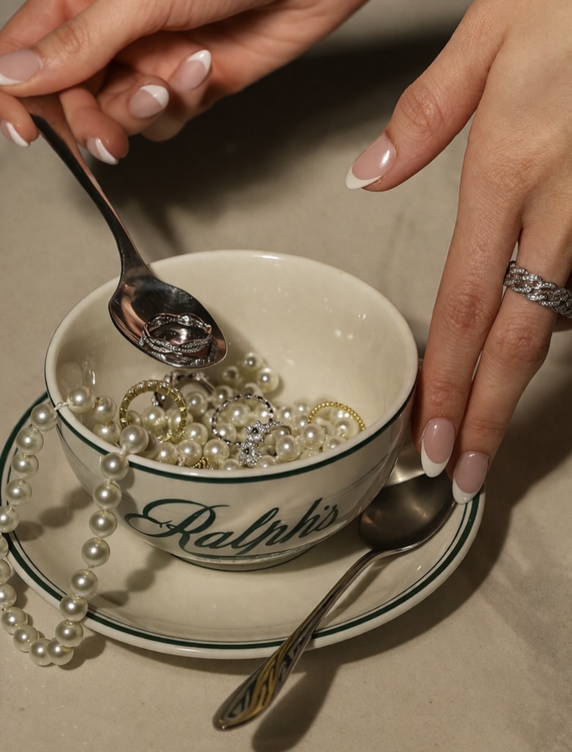 Styled jewelry flat lay in a Ralph's teacup with pearls, rings, and manicured hands