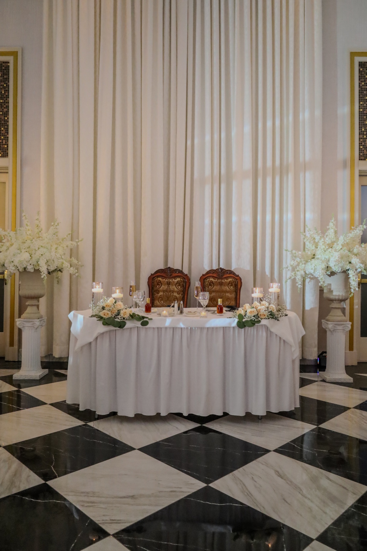 Elegant sweetheart table with white florals on a checkered marble floor