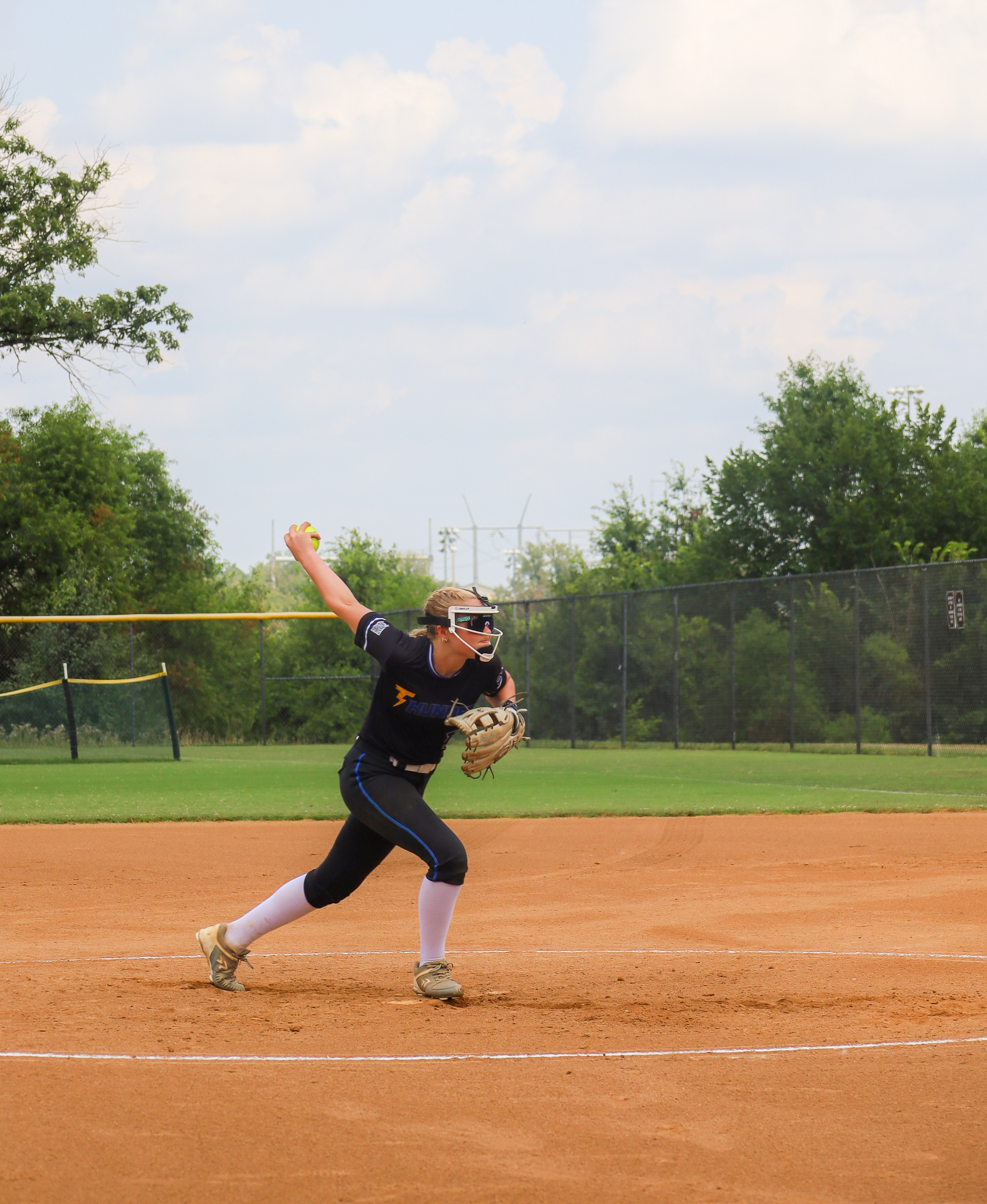 Softball pitcher in black Thunder jersey releasing a pitch