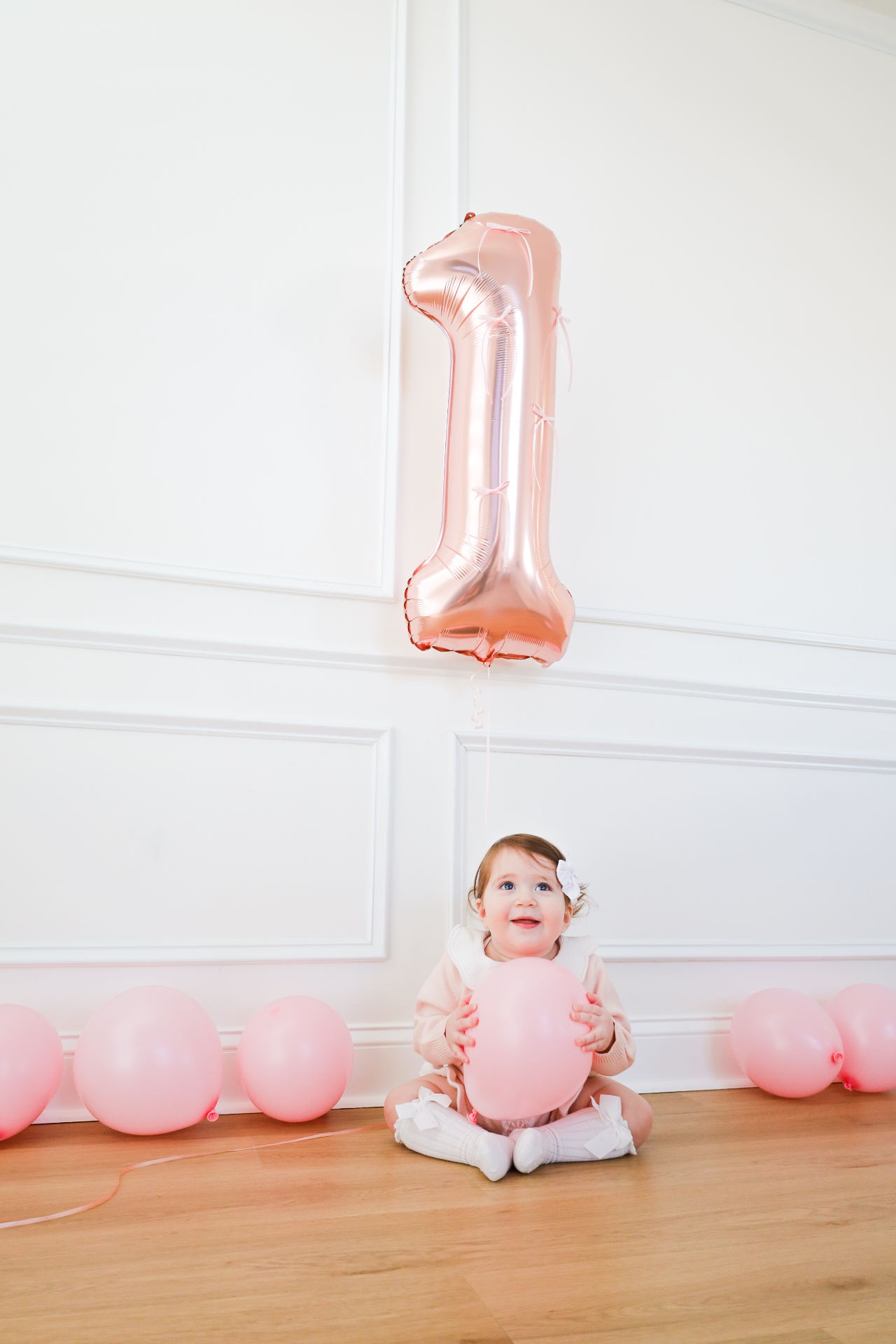 Baby girl sitting beneath a rose gold number one balloon with pink balloons for a first birthday session